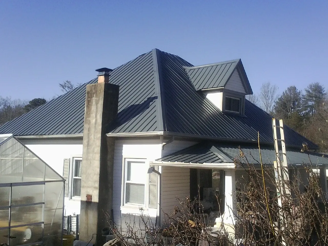 Dark blue standing seam metal roof on a white farmhouse with dormer — Slate & Tile Roof Repair by Roofing Brothers in Fraser