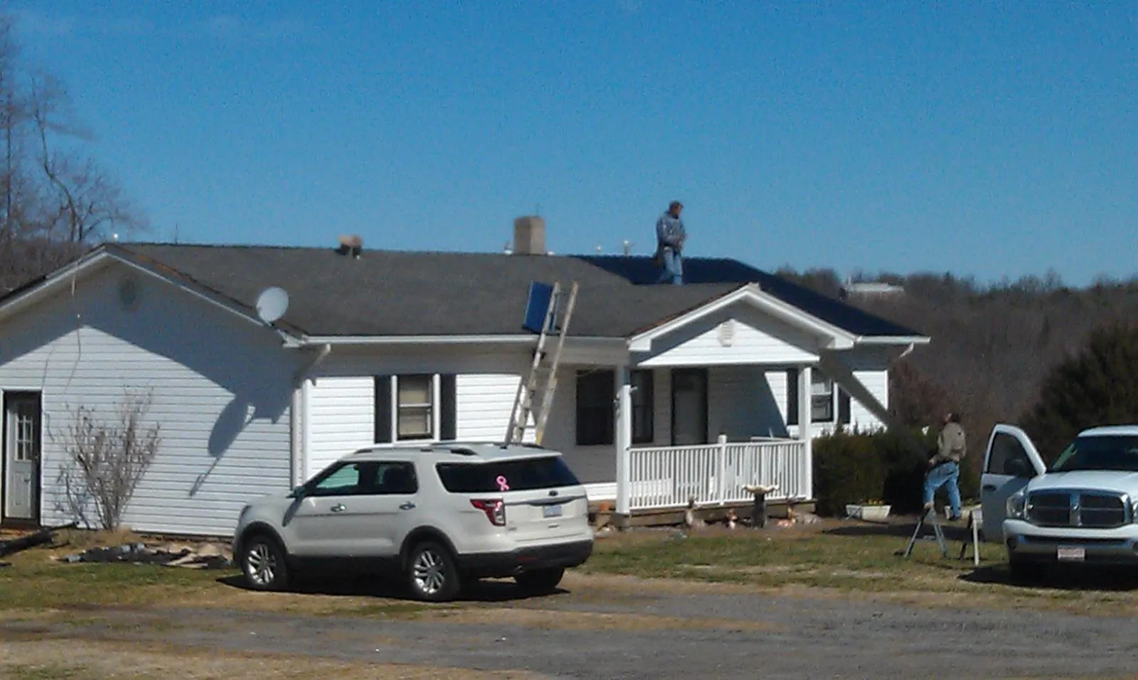 Roofers stripping shingles from a white ranch house roof in Fraser