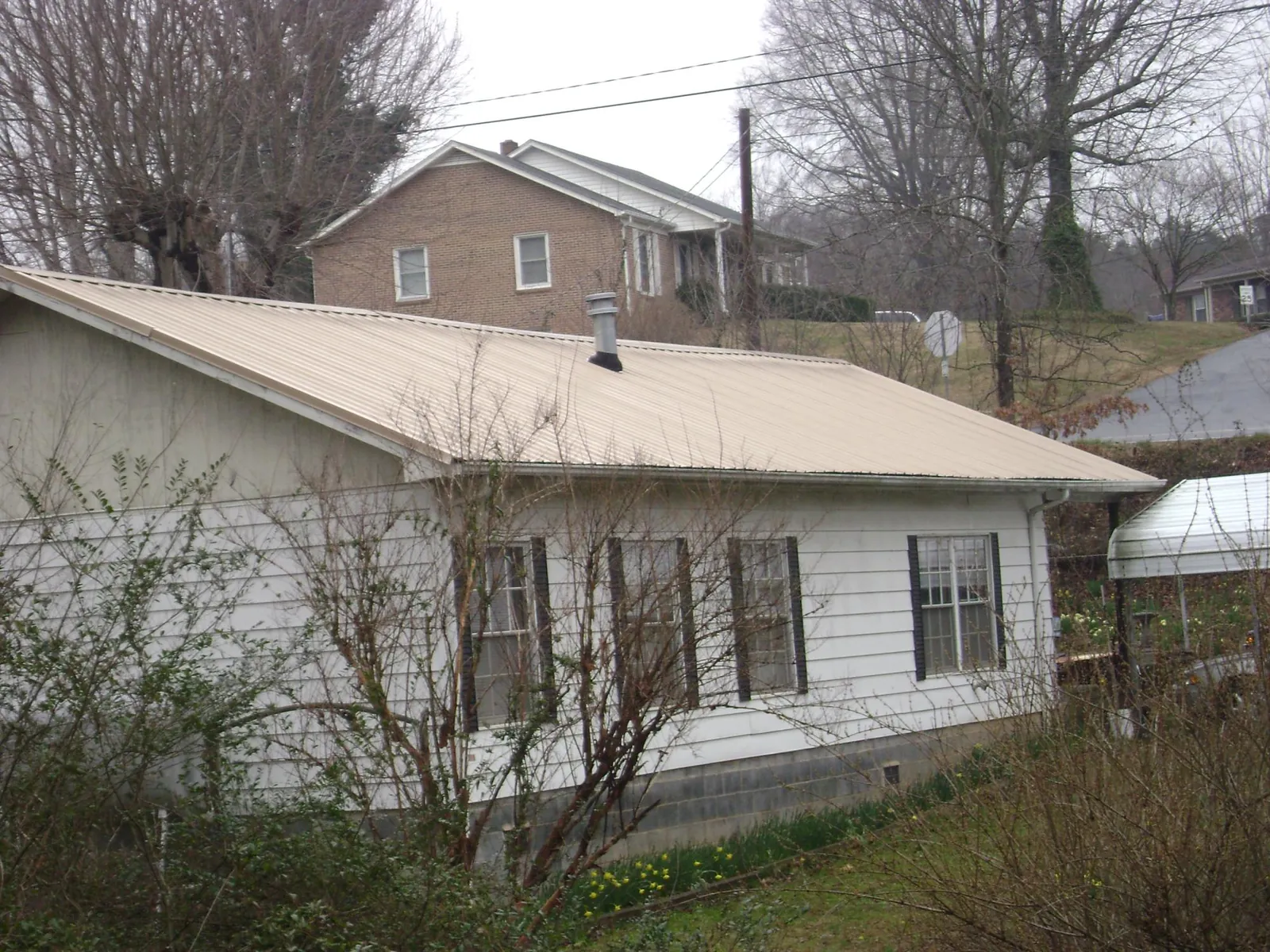 Tan metal roof on a white sided house set into a hillside — Commercial Roofing by Roofing Brothers in Fraser